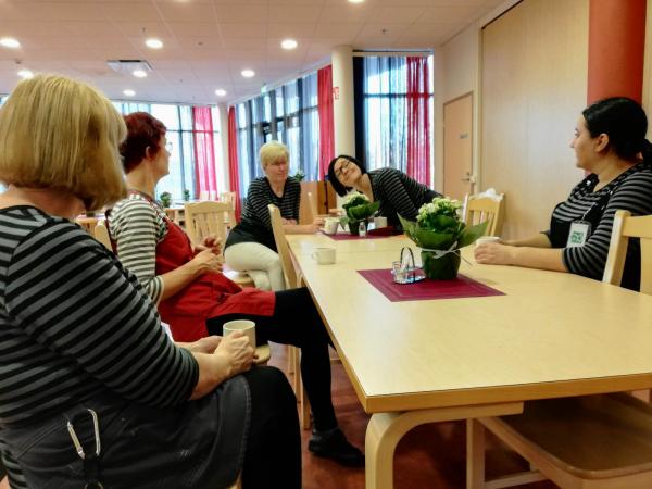 naiset istuvat pöydän ympärillä ja juovat kahvia