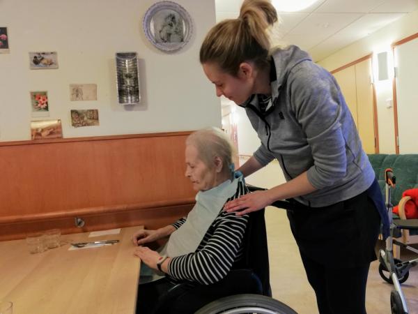 Hoitaja auttaa ruokalapun ikäihmiselle